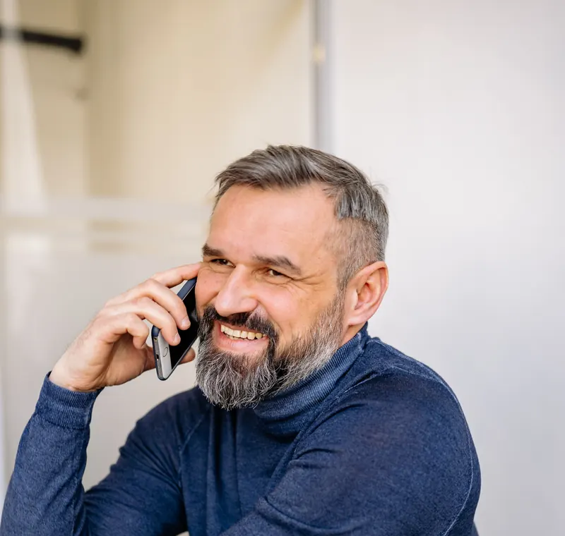 Ramus barzdotas vyras šiltai šypsodamasis kalba telefonu namuose